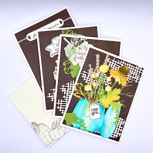 May include: A collection of handmade greeting cards with a fall theme. The cards feature embossed brown backgrounds with white borders and decorative cutouts. One card has a turquoise pumpkin with a "Thank You" tag. Other cards have text that reads "Just because", "I love", and "Happy Birthday".