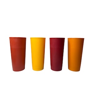 May include: A set of four cylindrical drinking tumblers in solid colors. The tumblers are arranged in a row, featuring a deep red, a bright yellow, a dark maroon, and a vibrant orange finish. Each cup has a smooth, matte texture.