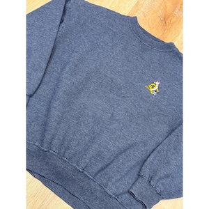 May include: A blue crew neck sweatshirt with a small embroidered design of a cartoon character playing soccer. The sweatshirt has a ribbed texture and ribbed cuffs and hem. The fabric appears to be a medium weight.