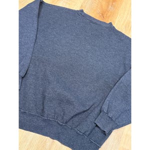 May include: A navy blue crew neck sweatshirt with a ribbed texture. The long-sleeved top has ribbed cuffs and a ribbed hem. The fabric has a subtle striped pattern. The sweatshirt is made of a soft, comfortable material.