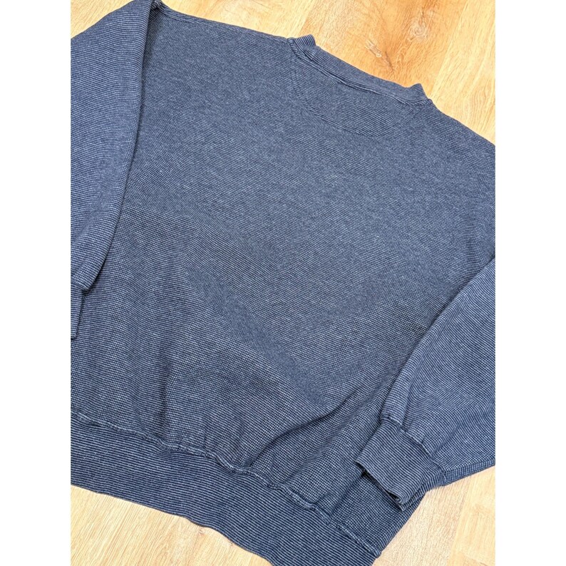 May include: A navy blue crew neck sweatshirt with a ribbed texture. The long-sleeved top has ribbed cuffs and a ribbed hem. The fabric has a subtle striped pattern. The sweatshirt is made of a soft, comfortable material.