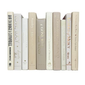 May include: A collection of ten hardcover books arranged vertically, featuring spines in neutral shades of cream, beige, tan, and off-white. The titles include How to Dodge a Cannonball, Love, Lucy, Sooley, Gone with the Wind, A Question of Betrayal, The Grimaldi of Monaco, Rainwater, and Eclipse of Mercy.