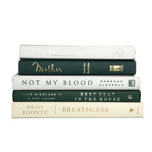 May include: A stack of five hardcover books with spines facing forward. The books feature alternating cream and dark green covers with gold and black text, including titles such as Mother, Not My Blood, Best Seat in the House, and Breathless.