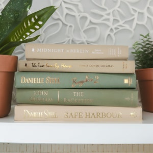 May include: A stack of five books with green and beige covers. The titles of the books are "Midnight in Berlin", "The Two-Family House", "Bungalow 2", "The Racketeer", and "Safe Harbour".