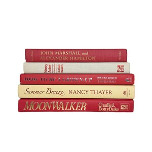 May include: A stack of five hardcover books with spines facing forward. The top book is red with gold text, followed by a beige book, a red book with silver text, a cream book with black text, and a red book with gold text at the bottom.
