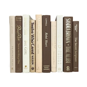 May include: A collection of hardcover books with various titles and authors, in shades of brown, beige, and white. The spines are visible, showcasing the titles and author names. The books are arranged vertically.