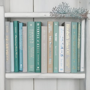 May include: A bookshelf with a variety of books in shades of blue and green. The books have gold lettering on the spines and are arranged in a row. The bookshelf is white and has a decorative coral branch on top.