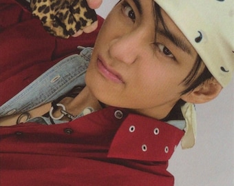 May include: A red button-down shirt with silver eyelets on the collar, worn over a light blue denim jacket. The outfit includes a cream-colored bandana with a small black graphic print and a fingerless glove featuring a brown and black leopard print.