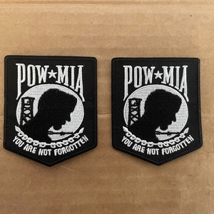 May include: Two black embroidered patches with white stitching. Each patch features a silhouette of a person's head with a building behind them. The text "POW*MIA YOU ARE NOT FORGOTTEN" is written on each patch.