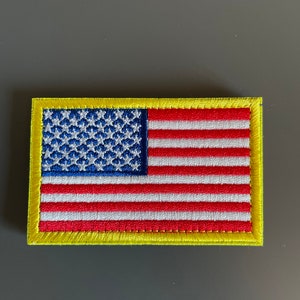 May include: A small embroidered American flag patch with a yellow border. The flag is red, white, and blue.