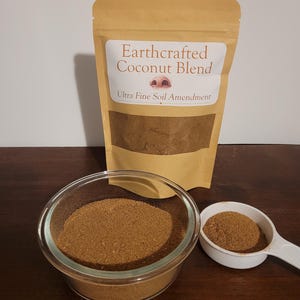 May include: A tan pouch labeled Earthcrafted Coconut Blend Ultra Fine Soil Amendment containing brown powder. A clear glass bowl filled with the same brown powder sits in front, accompanied by a white plastic measuring scoop filled with the powder.