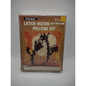 May include: A Perlon Latch Hook Pillow Kit, model PK-8020 "Sunset". The kit includes a pillow cover, acrylic yarn, pre-printed canvas, and instructions. The pillow design features a sunset color scheme with orange, brown, and white hues. The finished pillow size is 12" x 12".