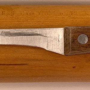 May include: A stainless steel boning knife with a curved blade and a dark brown wooden handle. The knife is resting on a light brown wooden surface. The handle is secured with two silver rivets.