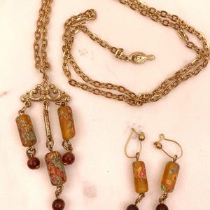 May include: A vintage gold-tone necklace and matching earrings set. The necklace features a decorative pendant with three cylindrical beads and three small red beads. The earrings have a similar design with cylindrical beads and red beads.