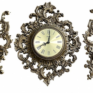 May include: Ornate antique-style wall clock with matching sconces. The clock features a round face with Roman numerals and decorative hands, surrounded by an elaborate gold-toned frame. The sconces have a similar design, creating a cohesive set.