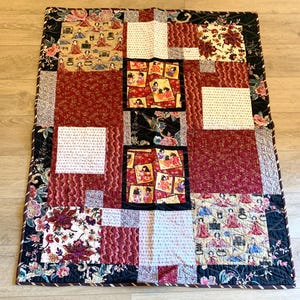 May include: A patchwork quilt with a variety of patterns and colors. The quilt features squares of red, white, and black fabric with floral and geometric designs. The border is a dark floral print.