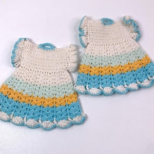 Puede incluir: Dos vestidos de ganchillo en blanco, azul y amarillo. Los vestidos tienen un borde festoneado y están hechos con un punto delicado.