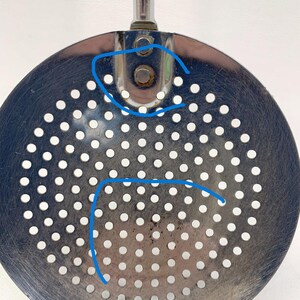 May include: A silver-colored metal slotted spoon with a handle. The spoon has a circular, perforated surface with a pattern of small holes. The spoon has the text "EKCO U.S.A." printed on the bottom.