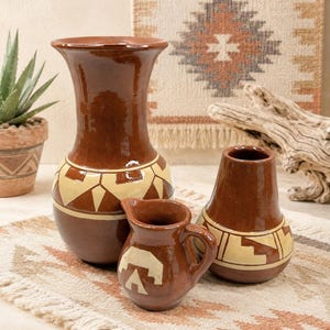 Peut inclure: Ensemble de vases en céramique marron et un petit pichet avec des motifs géométriques crème. Les vases varient en taille et en forme, avec un grand vase évasé et un plus petit, arrondi. Le pichet a une anse et un motif d'ours.