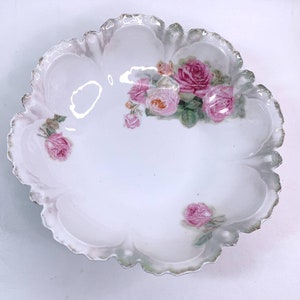 May include: A white porcelain bowl with a scalloped edge and a floral design featuring pink roses. The bowl is decorated with a delicate gold trim.