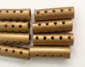 May include: Eight gold hair rollers with holes and the text "JAPAN" printed on two of the rollers. A single black metal hair clip is also included.