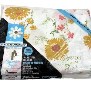 May include: A white twin bed fitted sheet in plastic packaging featuring a floral pattern with yellow and pink flowers. The label reads Penn-Prest, Fashion Manor, 50% polyester, 50% cotton, no-iron muslin, and 39 x 75 inches for a twin bed.