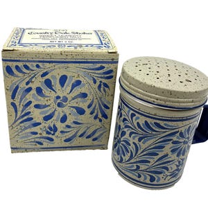 May include: An Avon Country Tale Shaker for Sweet Honesty perfumed talc, featuring a cream-coloured container with blue floral patterns and a speckled finish. The set includes a matching square cardboard box with the text Net Wt 3 oz printed on top.