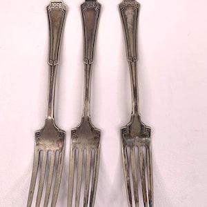 May include: Three silver forks with ornate handles. The handles have a geometric design and the tines are pointed.