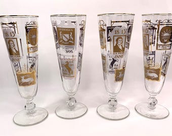 May include: Set of four vintage gold-rimmed glasses with a gold and white design featuring various signs and text. The signs include "On Pear Inn", "D. Beeme 1845", "H.A. Whi", and "Seekman 1845".