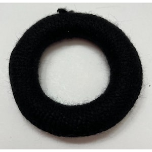 May include: A black, circular hair tie made of a soft, textured material. The hair accessory is a solid black color and appears to be made of a knitted or woven fabric. The hair tie is designed to hold hair in place.