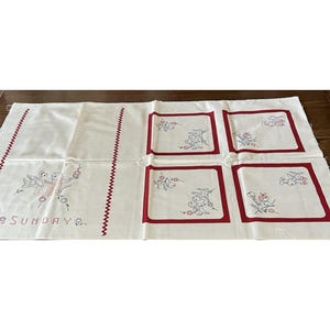 May include: A white rectangular fabric panel featuring red embroidered borders and decorative stitching. The design includes blue and red bird motifs, floral accents, and the word SUNDAY embroidered in a cross-stitch style on the left side.