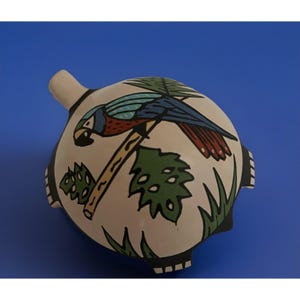 May include: A ceramic, round-shaped decorative item with a parrot design. The parrot is perched on a branch, with blue, red, and green details. The item has a beige base with black accents and green foliage.
