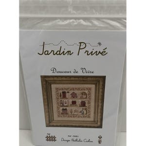 May include: A cross-stitch pattern kit titled Jardin Privé Douceur de Vivre by Nathalie Cichon, reference DM01. The packaging features a printed image of a nine-square grid embroidery design depicting houses and trees in a wooden frame.