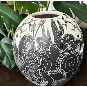 May include: Black and white ceramic vase with a Day of the Dead theme. The vase features detailed illustrations of skeletons, tombstones, and the text "RIP" and names. The design is carved into the surface, creating a striking contrast.
