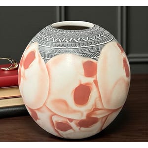 May include: A round ceramic vase with a white and red skull design. The top of the vase features a black and white geometric pattern. The vase is sitting on a dark wooden surface.
