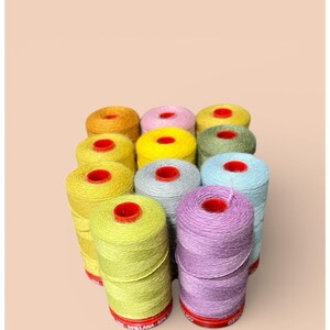 May include: A collection of colorful spools of yarn, each with a red center. The yarn colors include yellow, pink, green, blue, and purple. The spools are arranged closely together, creating a vibrant display of crafting supplies.