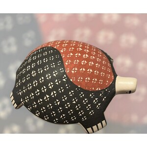May include: A ceramic armadillo figurine with a distinctive design. The body is primarily black with a repeating white cross pattern. The back features a reddish-brown section with a similar white cross pattern. The snout is white.