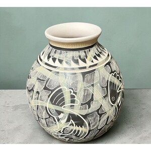 May include: A round ceramic vase featuring a matte black surface decorated with white etched bird motifs and geometric patterns. The vessel has a wide, light-colored rim and a bulbous body covered in intricate, hand-drawn white line work.