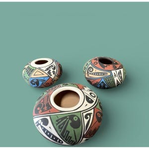 May include: Three round, hand-painted ceramic vases with a wide opening. The vases feature a colorful geometric design with black, red, green, blue, and white accents. The vases are arranged on a teal background.