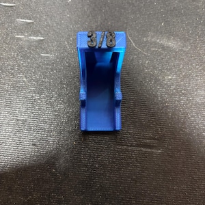 Puede incluir: Un objeto azul impreso en 3D con el texto "3/8" en la parte superior. El objeto tiene forma rectangular con un centro abierto y dos peque&ntilde;as protuberancias en los lados. Probablemente sea una herramienta o una pieza para un ensamblaje m&aacute;s grande.