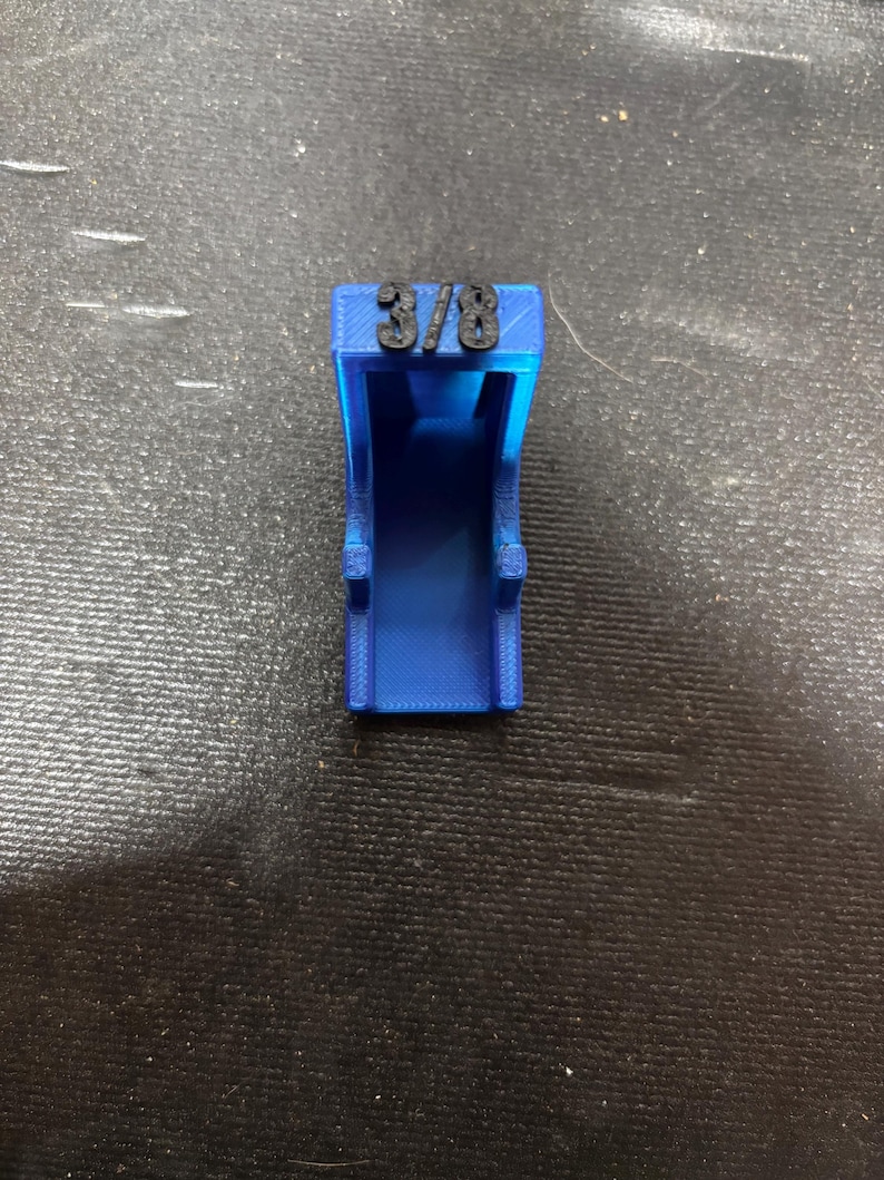 Puede incluir: Un objeto azul impreso en 3D con el texto "3/8" en la parte superior. El objeto tiene forma rectangular con un centro abierto y dos peque&ntilde;as protuberancias en los lados. Probablemente sea una herramienta o una pieza para un ensamblaje m&aacute;s grande.