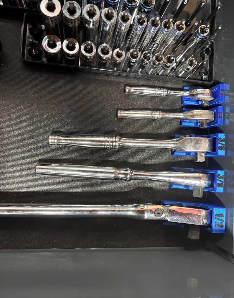 Puede incluir: Un conjunto de llaves de carraca y vasos cromados, cuidadosamente organizados en una bandeja negra. Las llaves de carraca est&aacute;n en soportes azules, con tama&ntilde;os etiquetados. Los vasos est&aacute;n alineados, listos para usar. Un juego pr&aacute;ctico para trabajos de automoci&oacute;n o mec&aacute;nica.