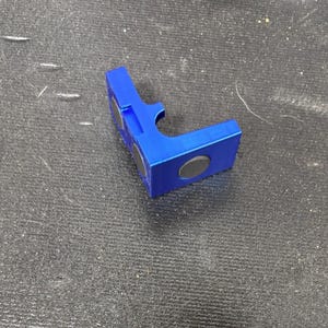 Puede incluir: Un objeto azul brillante en forma de L con dos imanes negros circulares adheridos. El objeto tiene un recorte curvo en un lado y parece estar hecho de pl&aacute;stico o un material similar. Descansa sobre una superficie oscura y texturizada.