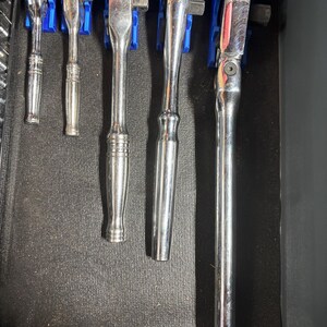 Puede incluir: Un conjunto de llaves de carraca plateadas de varios tama&ntilde;os, organizadas en soportes azules. Las medidas son 3/8 y 1/2. Las herramientas est&aacute;n dispuestas en un caj&oacute;n oscuro, listas para usar.