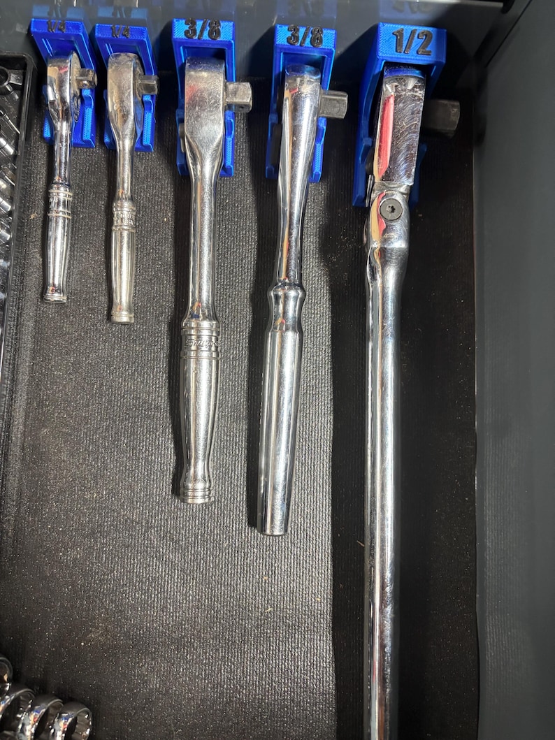 Puede incluir: Un conjunto de llaves de carraca plateadas de varios tama&ntilde;os, organizadas en soportes azules. Las medidas son 3/8 y 1/2. Las herramientas est&aacute;n dispuestas en un caj&oacute;n oscuro, listas para usar.