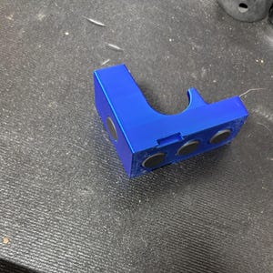 Puede incluir: Un soporte azul brillante en &aacute;ngulo recto con tres imanes negros integrados. El soporte tiene una secci&oacute;n curva y una ranura. El objeto est&aacute; hecho de un material s&oacute;lido y se encuentra sobre una superficie oscura texturizada.