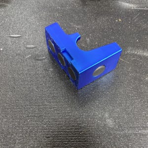 Puede incluir: Un objeto azul brillante y angular con tres imanes negros circulares incrustados en un lado y otro en otro. El objeto tiene un recorte curvo y parece estar hecho de pl&aacute;stico.