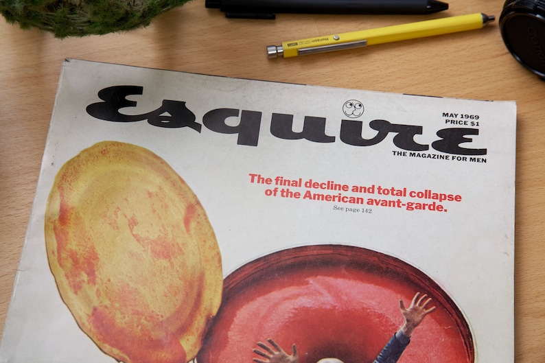 May include: A vintage magazine cover for Esquire magazine, featuring a red and yellow illustration of a person's hand reaching up from a large red circle. The cover text reads "Esquire" in bold black letters and "The final decline and total collapse of the American avant-garde. See page 142." The magazine cover is dated May 1969 and the price is $1.