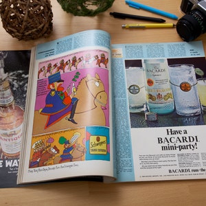 May include: An open magazine with a colorful illustration of a cartoon character riding a horse on the left page. The right page features a Bacardi rum ad with a bottle and two glasses of rum. The text on the ad reads "Have a Bacardi mini-party!" and "BACARDI - run the mixable one."