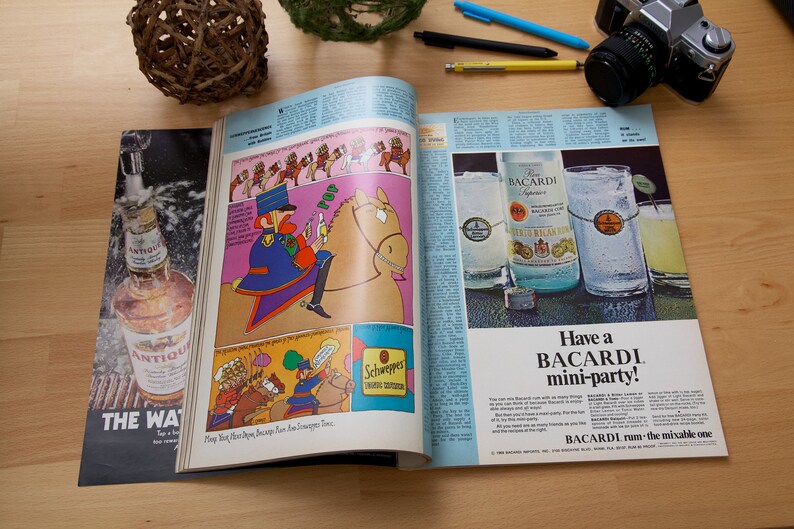 May include: An open magazine with a colorful illustration of a cartoon character riding a horse on the left page. The right page features a Bacardi rum ad with a bottle and two glasses of rum. The text on the ad reads "Have a Bacardi mini-party!" and "BACARDI - run the mixable one."